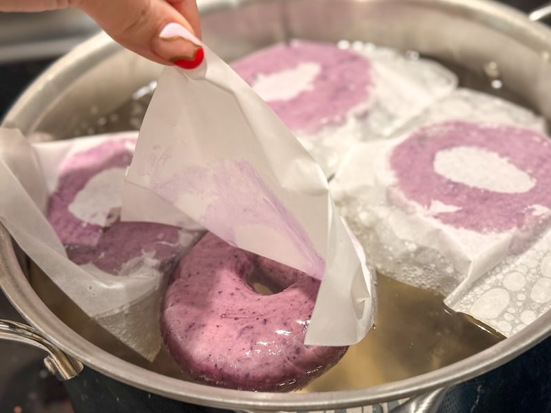 peeling parchment squares away as shaped bagels begin boiling in water