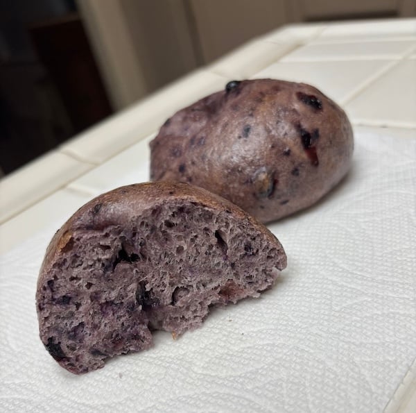 blueberry bagel with one cut half showing a dense purple crumb and visible blueberry pieces