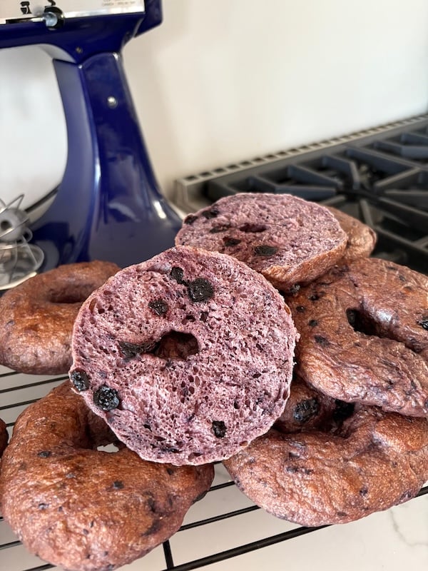 stack of blueberry bagels on a cooling rack with one sliced bagel showing the crumb