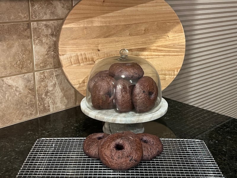 blueberry bagels displayed under a glass dome with three bagels in front
