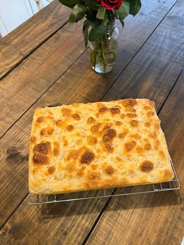 recipe tester square focaccia cooling on a wire rack, with a golden top and deep dimples