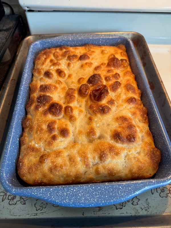 recipe tester focaccia baked in an enamel pan, with a deeply golden top and well-defined dimples