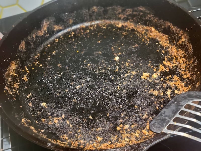 large cast iron skillet with browned crumbs and residue left behind from focaccia that stuck during baking