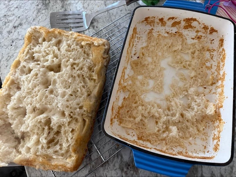 focaccia lifted out in one piece beside an enamel baking dish, showing much of the bottom crumb stuck in the pan