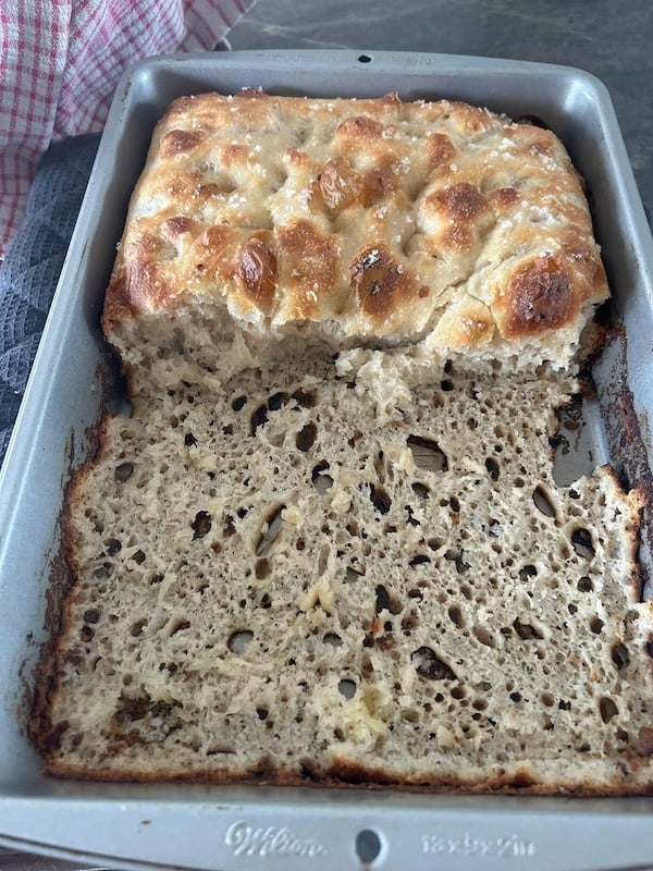 partially removed focaccia in a square metal pan, showing much of the bottom still stuck to the pan