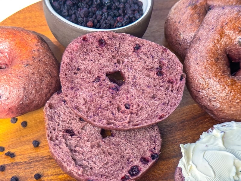 sliced wild blueberry sourdough bagel showing the purple crumb and dried blueberries, served with cream cheese