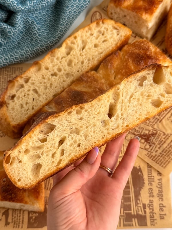 holding a thick slice of bubbly focaccia showing the open airy crumb