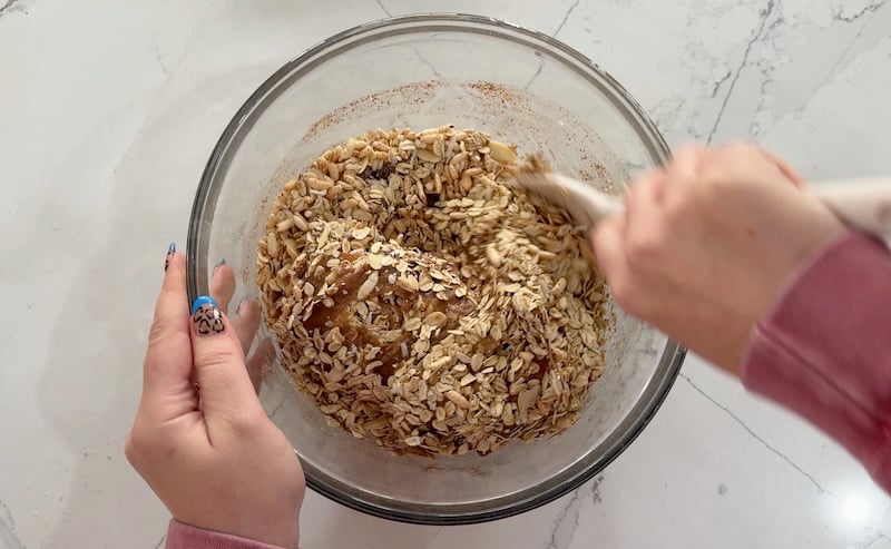 using a spatula to mix granola in large clear glass bowl