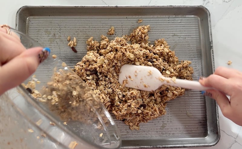 transferring granola mixture from bowl onto sheet pan