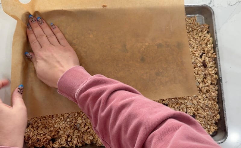 pressing granola mixture into pan using parchment paper
