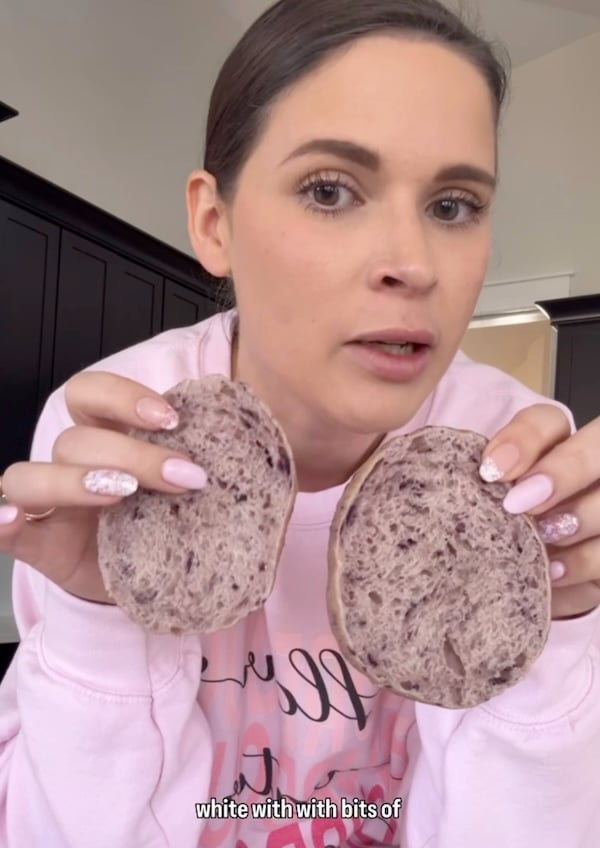 Rebekah holding a sliced blueberry sourdough bagel with a pale, tight crumb from early recipe testing