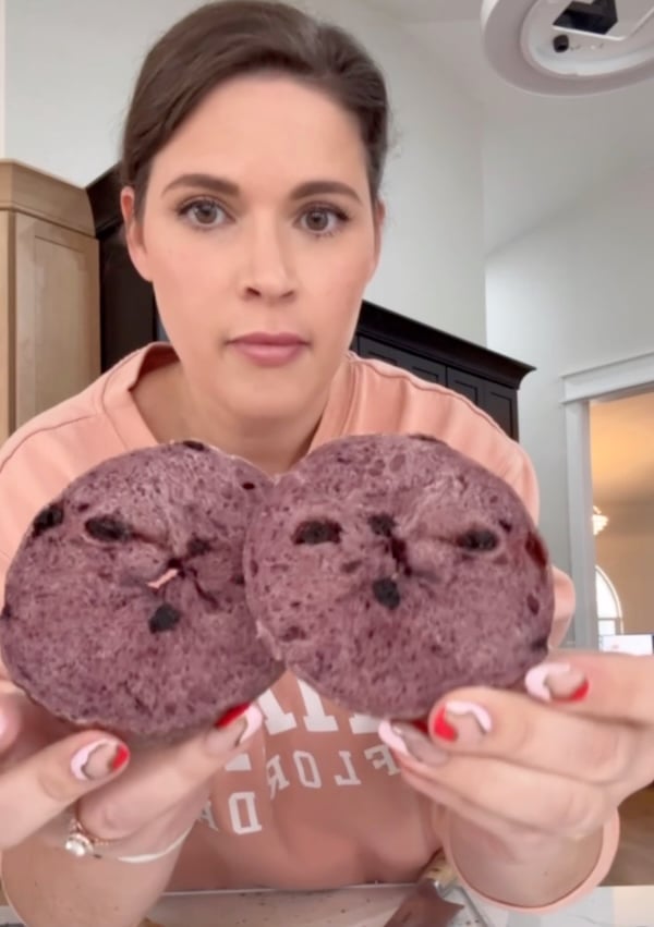 Rebekah holding two halves of a blueberry sourdough bagel with a dense purple crumb during testing