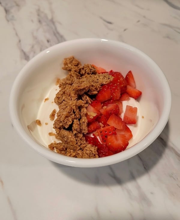 bowl of granola and sliced strawberries on top of yogurt