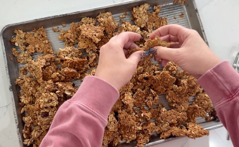 breaking baked granola clusters apart by hand on a sheet pan