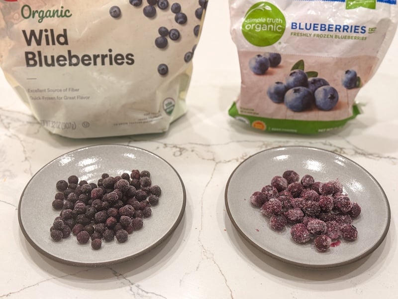 side by side comparison of frozen wild blueberries and regular frozen blueberries on plates with their bags behind them