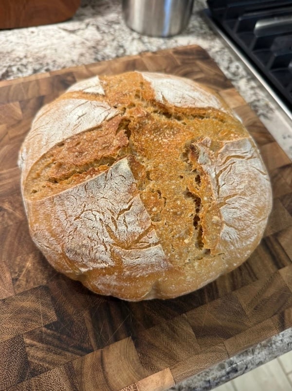 50% einkorn sourdough boule with an X score pattern, on a wooden cutting board