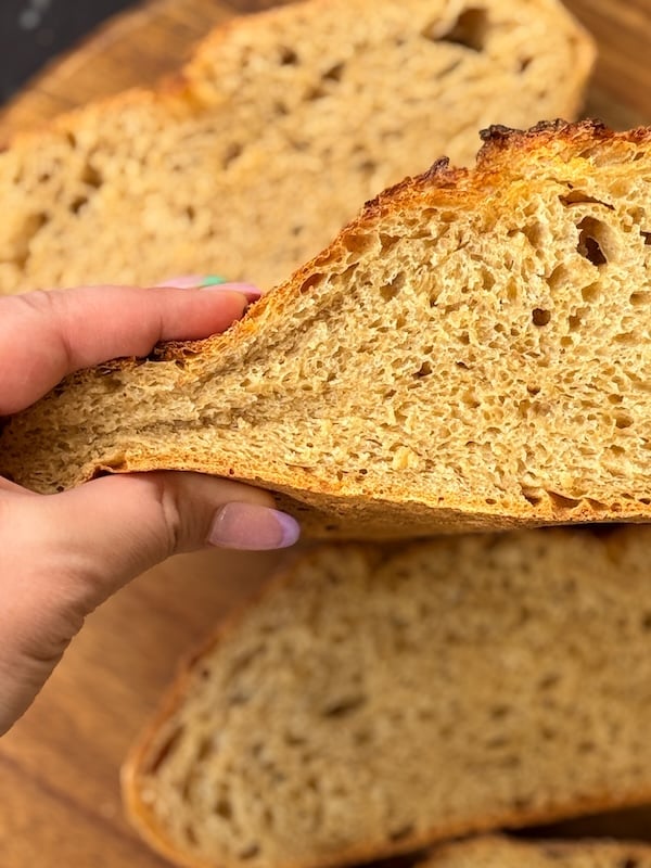 Slice of 50% einkorn sourdough bread held by hand to show the soft interior and open crumb