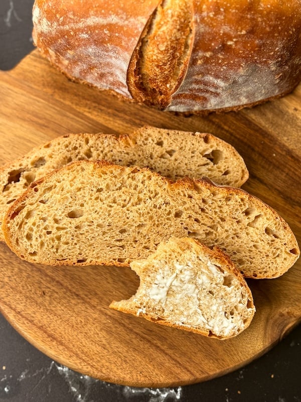 sliced 50% einkorn sourdough loaf on a cutting board with one piece spread with butter