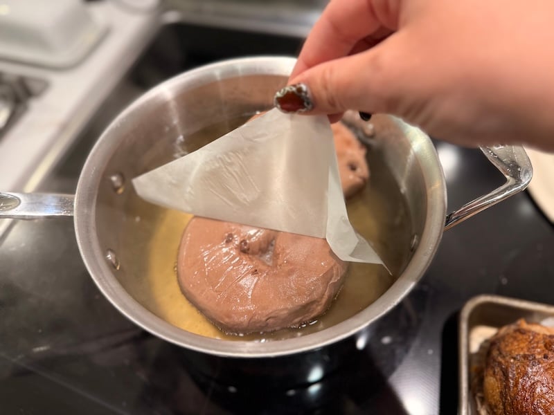 removing parchment from a chocolate bagel after lowering it in boiling water