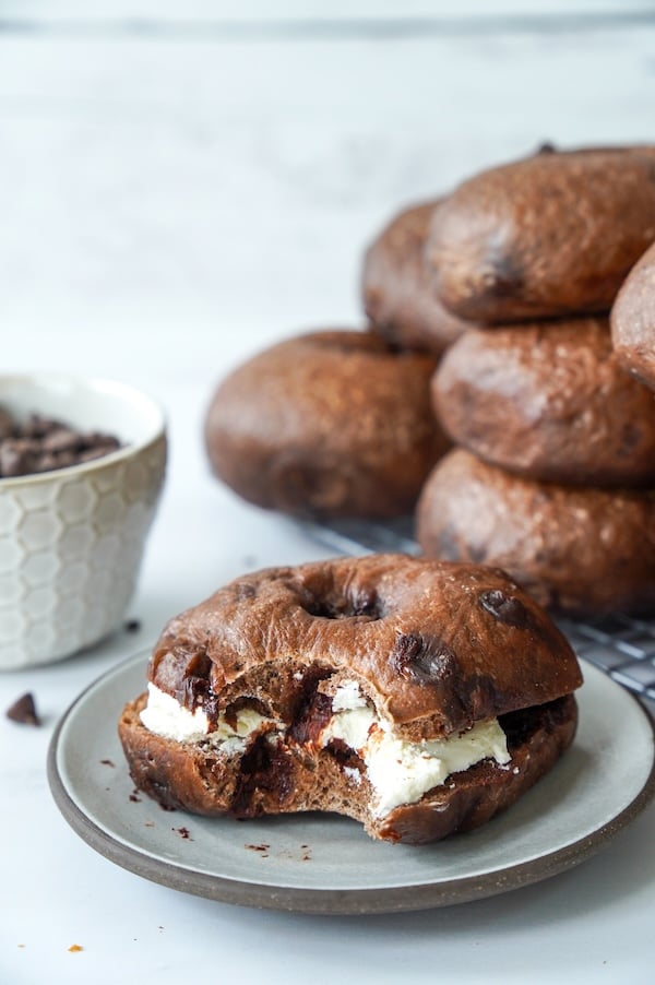 Double chocolate sourdough bagel sliced open and filled with cream cheese, with a stack of bagels in the background