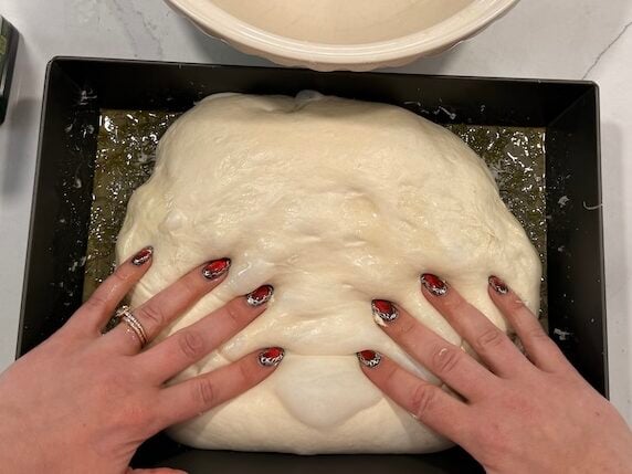 using your fingers to gently stretch the focaccia dough to the four corners of the pan