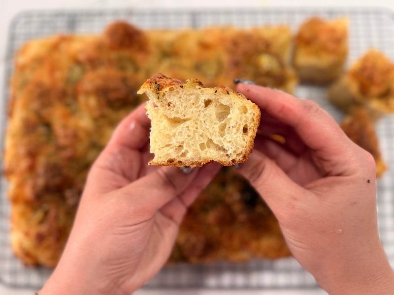 hands holding a sliced piece of roasted garlic and cheese sourdough focaccia