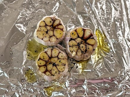 garlic heads on foil drizzled with oil before roasting