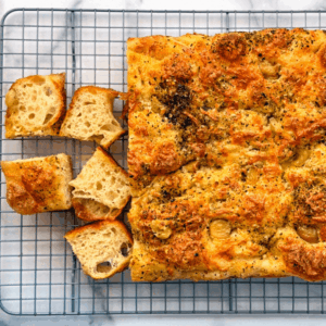sourdough garlic and cheese focaccia on a cooling rack with square slices