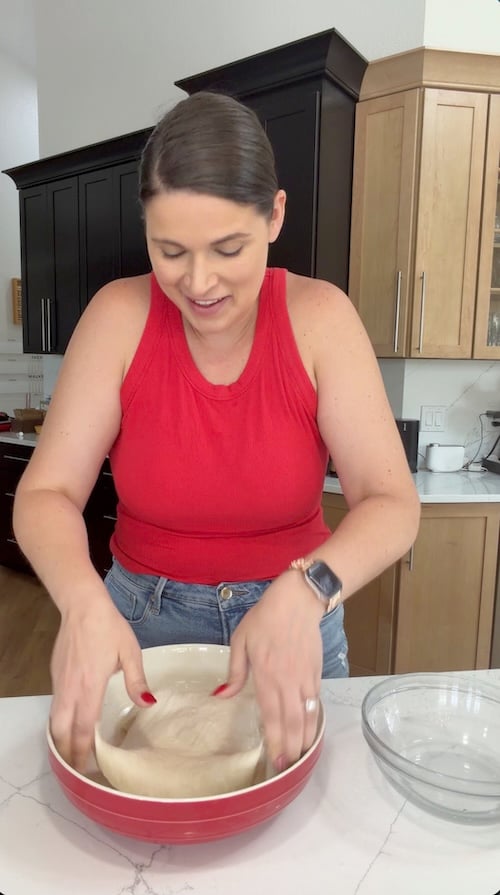 lowering stretched focaccia dough back into the bowl to complete a coil fold
