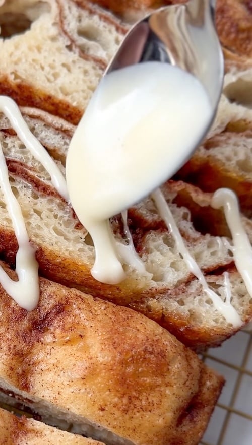 cream cheese drizzle being spooned over sliced cinnamon roll focaccia
