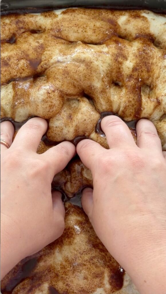 dimpling wet cinnamon butter mixture into focaccia