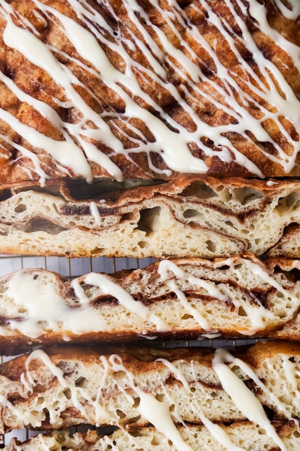 sliced cinnamon roll sourdough focaccia showing an airy crumb, cinnamon-sugar swirls, and white glaze