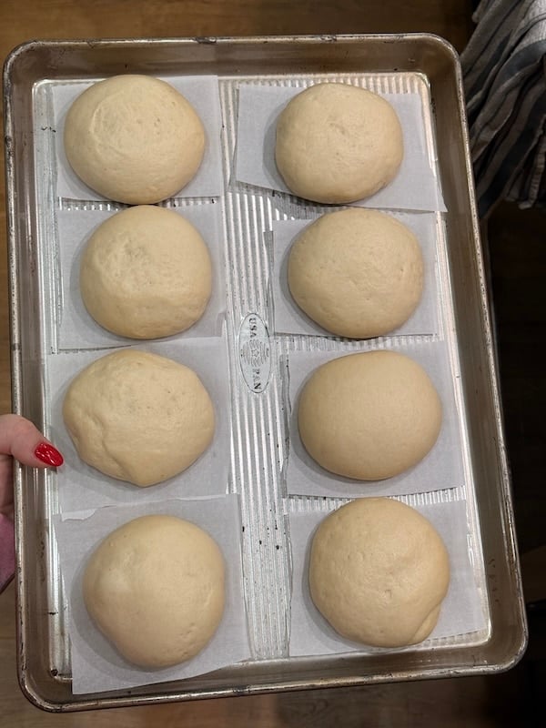 shaped pretzel buns atop individual parchment squares on a baking sheet tray