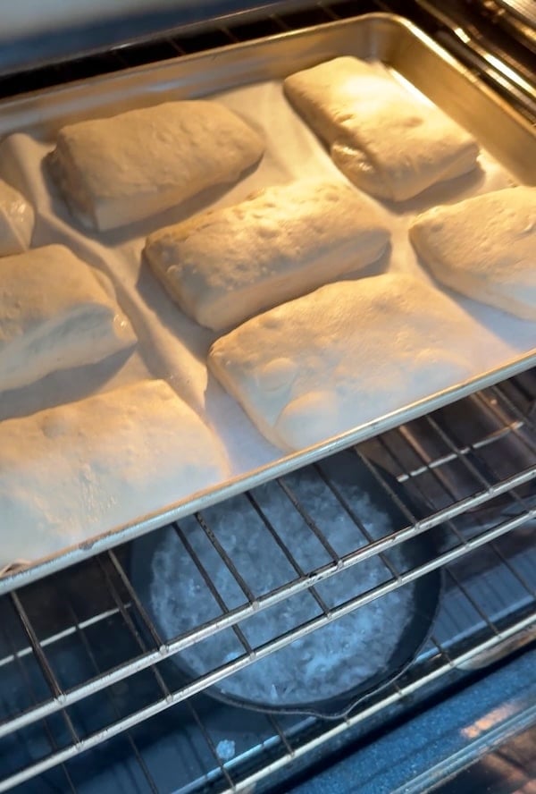 ciabatta rolls baking on a sheet pan with a steam skillet on the rack below