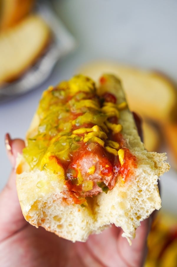 hand holding a hot dog in a sourdough Hawaiian bun with a bite taken out to reveal the airy crumb