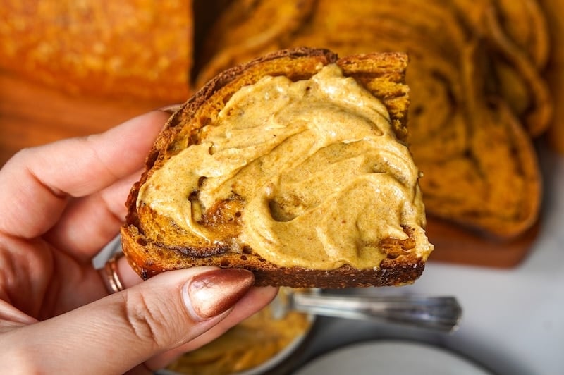 holding a half slice of pumpkin sourdough bread with pumpkin butter on top