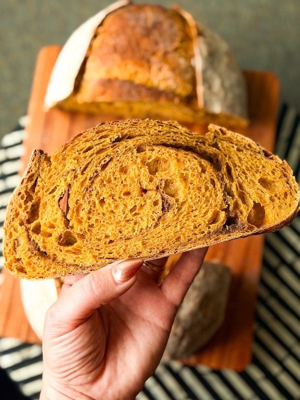 holding a slice of swirled pumpkin sourdough bread